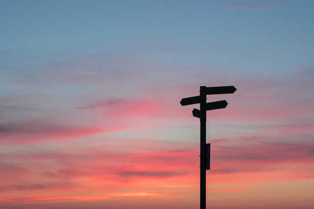 sun rising behind a directional sign