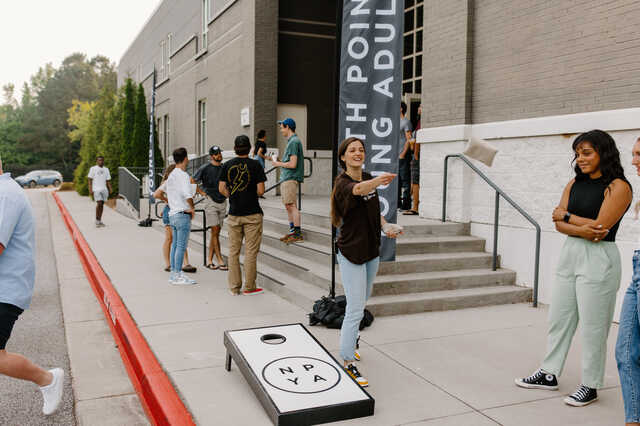 young adults playing cornhole outside the church building